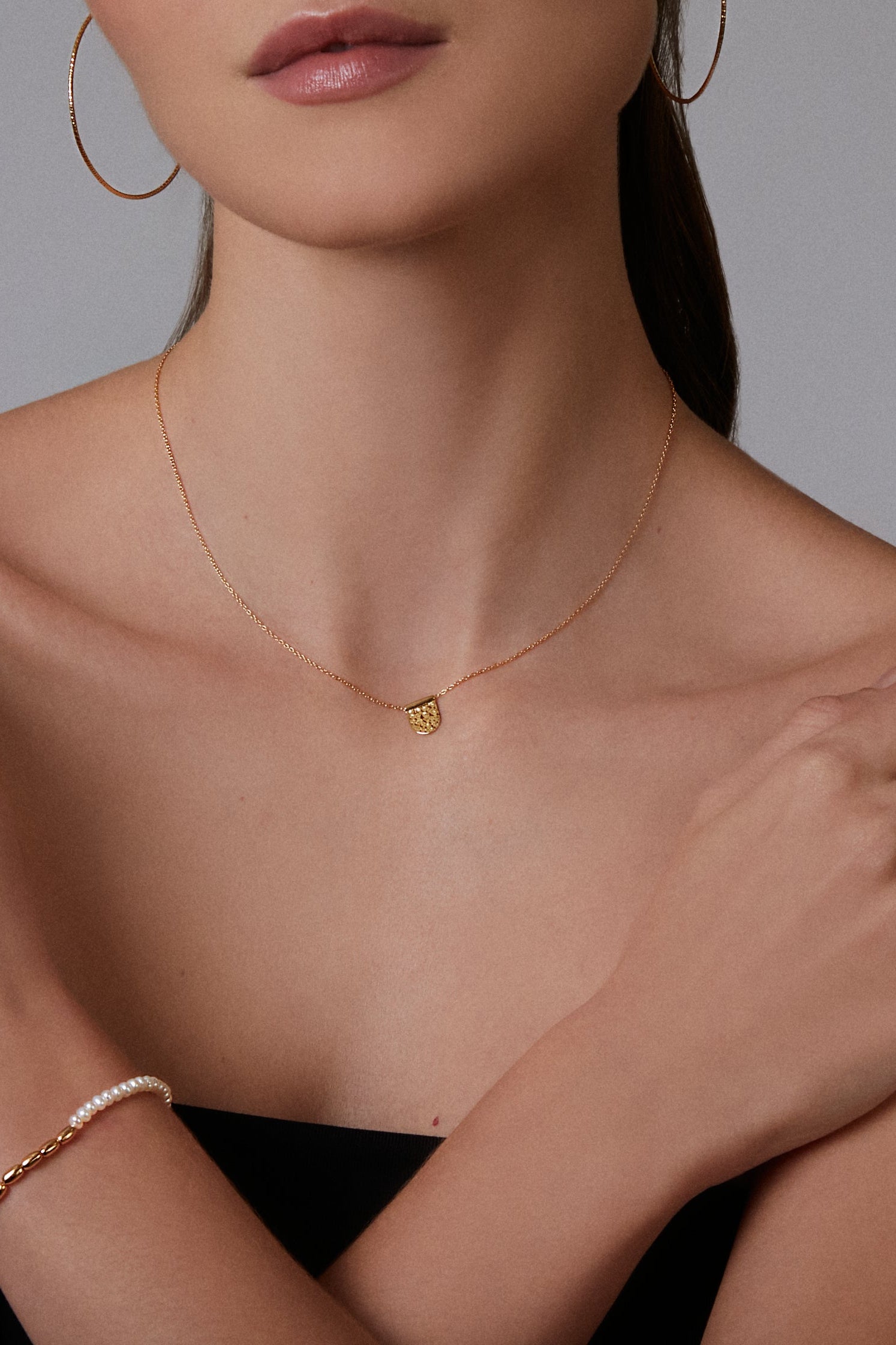 Woman wearing gold jewelry including a necklace, hoop earrings, and bracelet on a neutral background