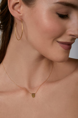 Close-up of a woman wearing gold hoop earrings and a necklace with a tag pendant.