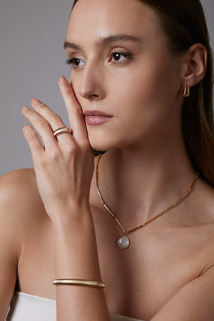 Woman wearing gold jewelry including a necklace, ring, and dome cuff bracelet against a neutral background