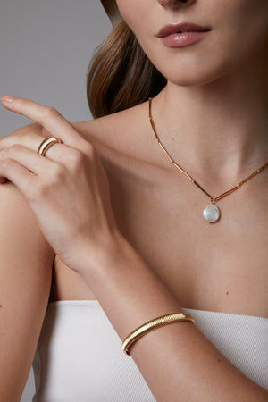 Close-up of a woman wearing gold jewelry including a necklace, ring, and bracelet.