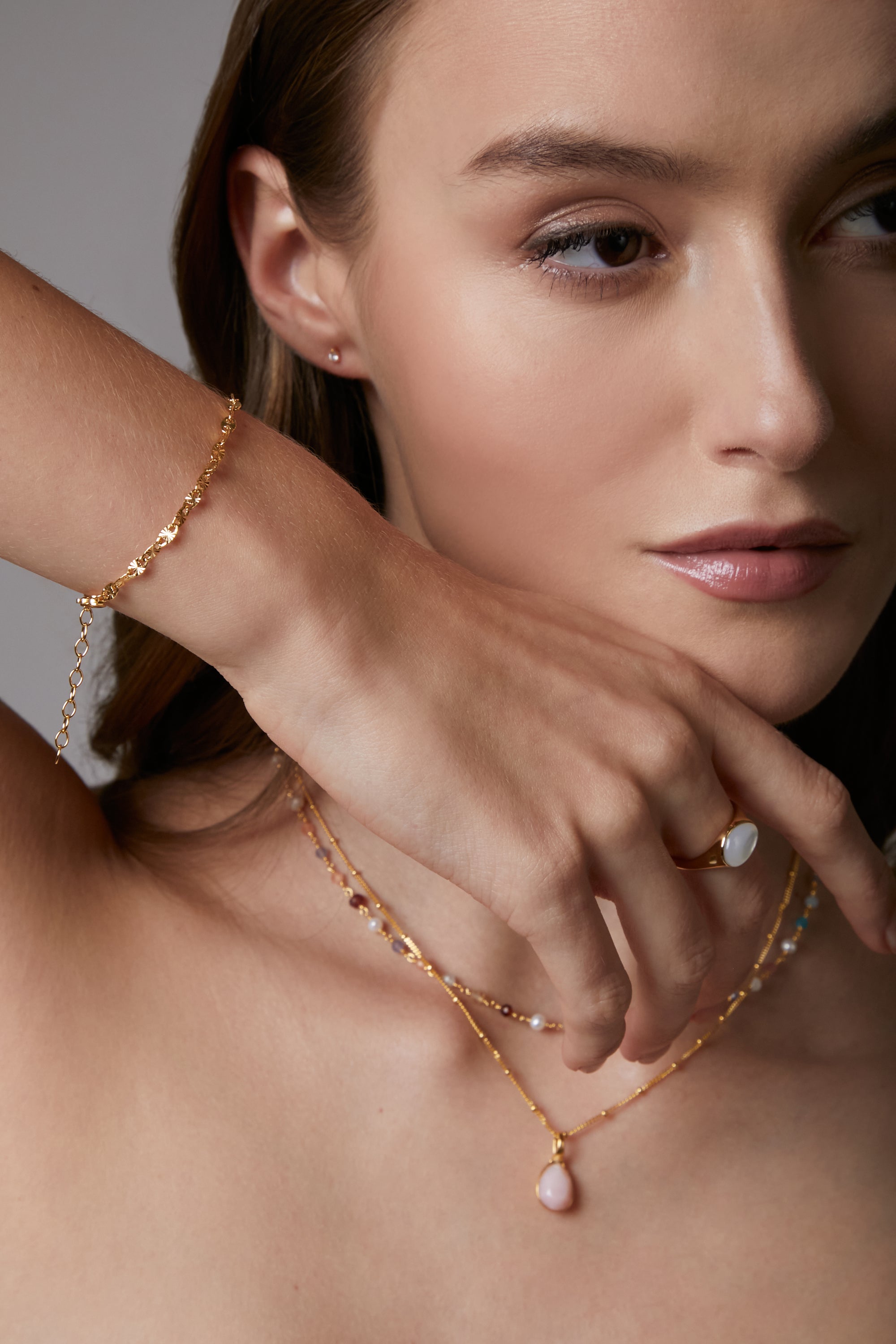 Woman wearing gold jewelry including a necklace, bracelet, and ring.