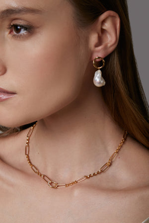 Close-up of a woman wearing gold hoop earrings with a pearl drop and a gold chain necklace.