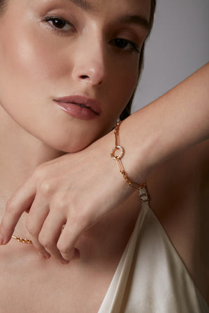 Close-up of a woman wearing a gold bracelet on a neutral background