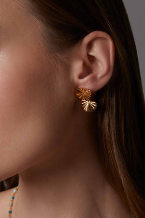 Close-up of a person wearing a gold leaf earring with a textured design.