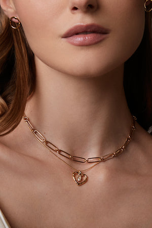 Woman wearing a gold necklace with a heart pendant against a neutral background