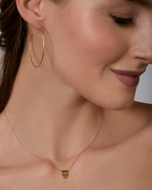 Close-up of a woman wearing gold hoop earrings and a necklace with a tag pendant.