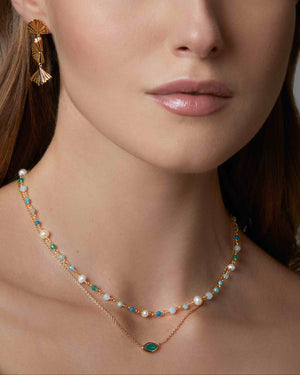 Woman wearing two green gemstone necklaces and leaf earrings against a neutral background