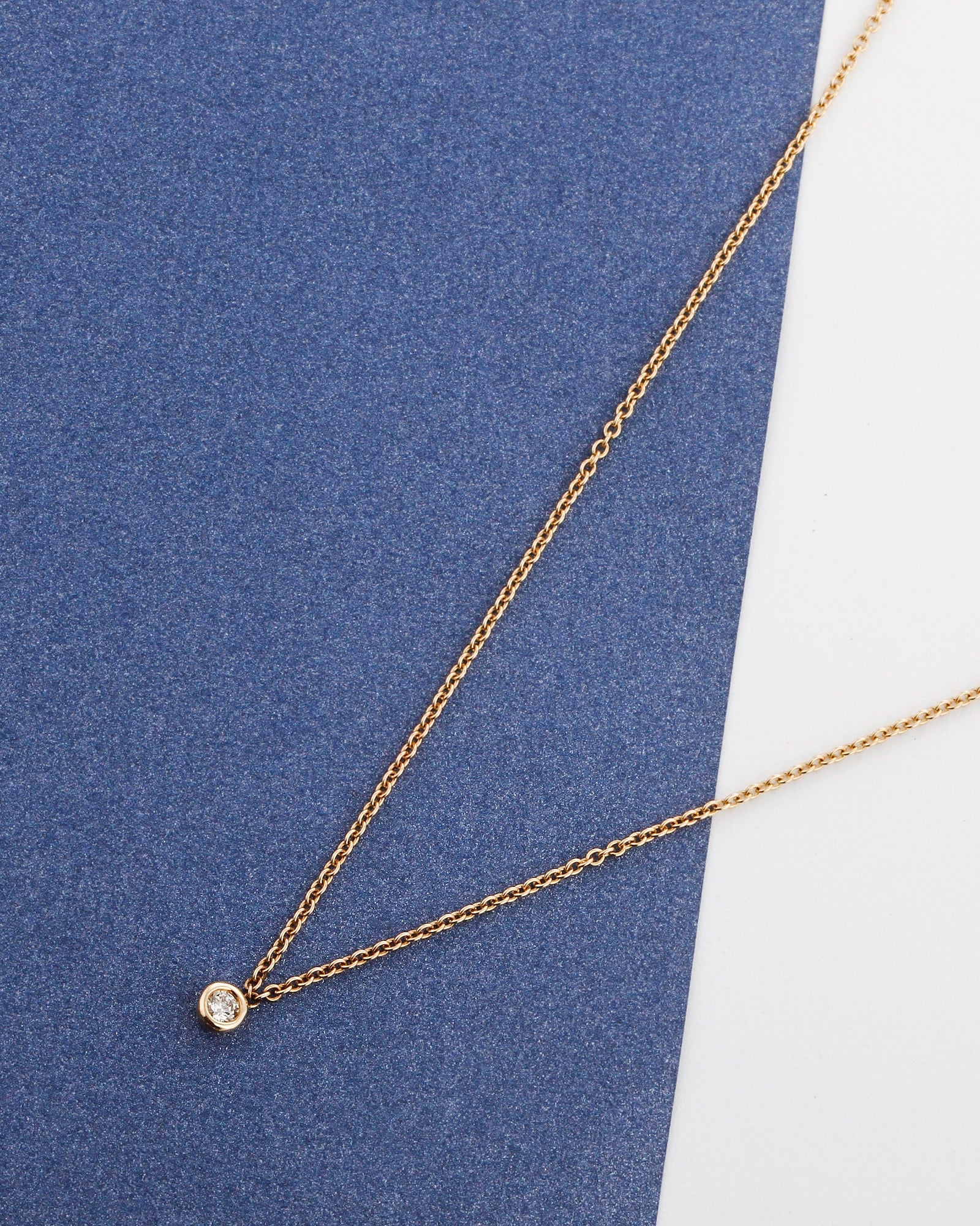 Gold dainty necklace with a diamond pendant on a white background