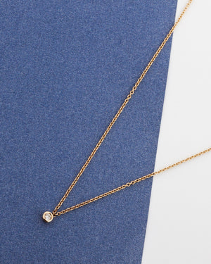 Gold solitaire diamond necklace with a small round pendant on a blue and white background