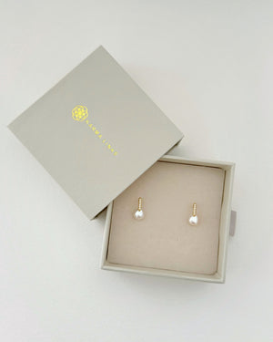 Pair of pearl earrings in an open jewelry box on a light gray background