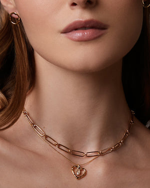 Woman wearing a gold necklace with a heart pendant against a neutral background