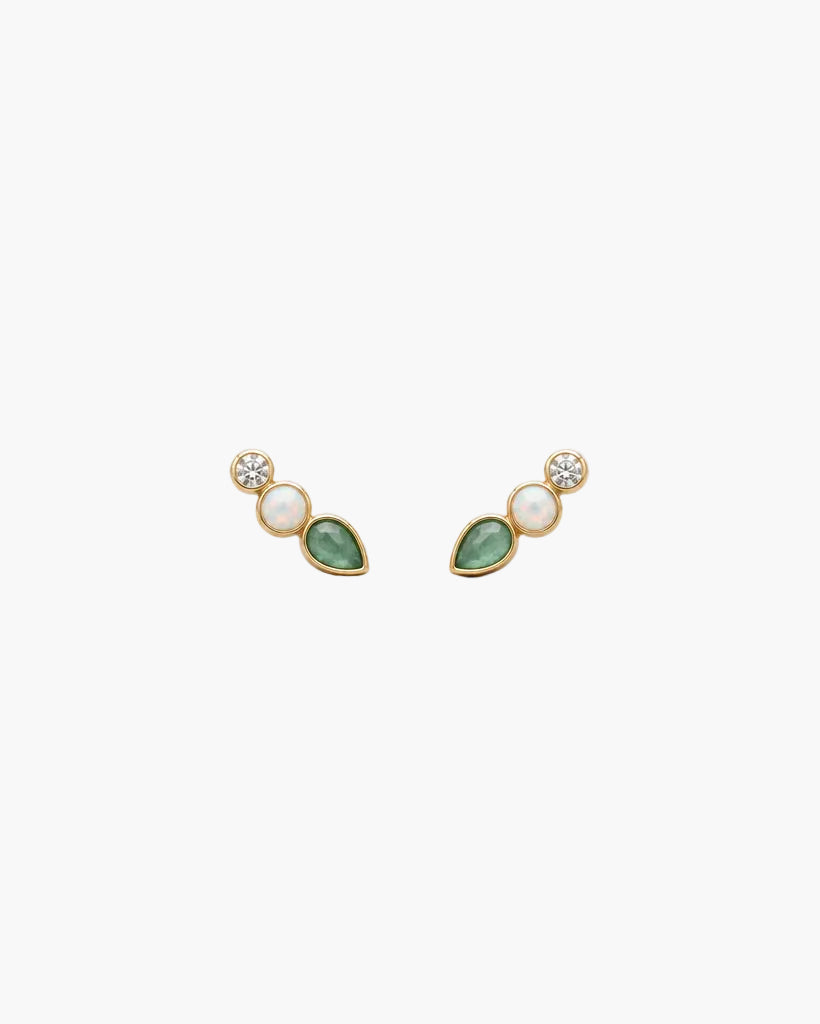 A pair of small gold-toned stud earrings on a textured off-white background. Each earring features a round clear stone, a small oval pale pink stone, and a teardrop-shaped green stone.