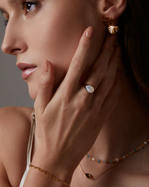 Close-up of a woman wearing gold earrings, ring, and bracelet against a neutral background