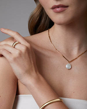 Close-up of a woman wearing gold jewelry including a necklace, ring, and bracelet.