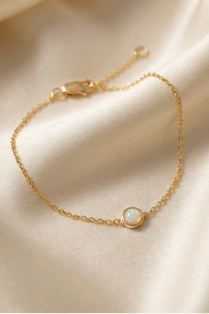 Gold bracelet with a small opal charm on a silk fabric background