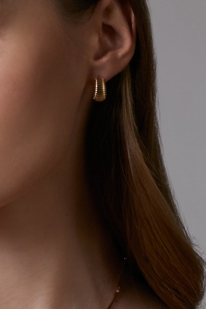 Close-up of a person wearing gold hoop earrings with a neutral background