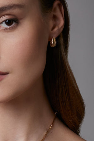 Close-up of a woman wearing gold hoop earrings with a neutral background