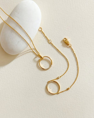 Gold necklace with circular pendants on a light beige background