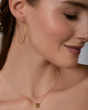 Close-up of a woman wearing large gold hoop earrings and a necklace with a tag pendant.