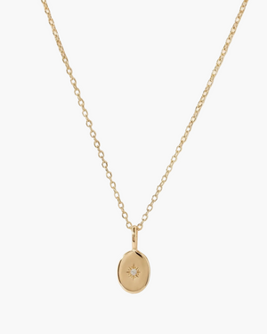 Gold necklace with a small pendant on a light beige background