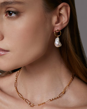 Close-up of a woman wearing gold hoop earrings with a pearl drop and a gold chain necklace.