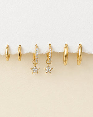 three pairs of gold hoop earrings, including one with small star charms displayed on a textured white surface.