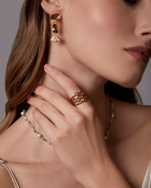 Woman wearing gold leaf asymmetrical leaf drop earrings with a triple green gemstone ring 