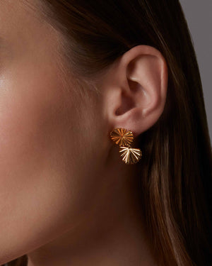 Close-up of a person wearing a gold leaf earring with a textured design.