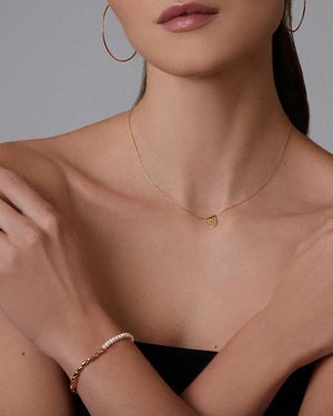 Woman wearing gold jewelry including a necklace, ring, and bracelet against a neutral background