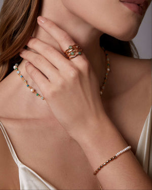 Close-up of a woman wearing gold earrings, ring, and bracelet against a neutral background