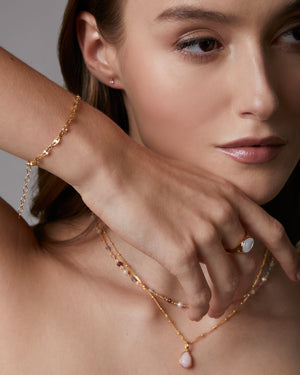 Close-up of a woman wearing gold jewelry including a necklace, bracelet, and ring.