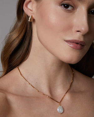 a woman wearing gold ridged dome hoop earrings and pearl necklace