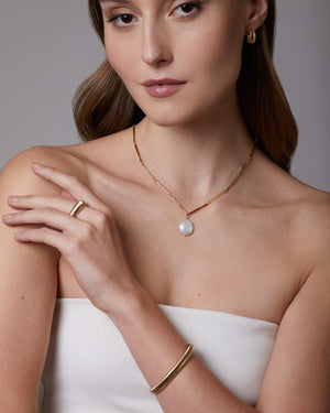 Woman wearing gold jewelry including a necklace, ring, and bracelet against a neutral background