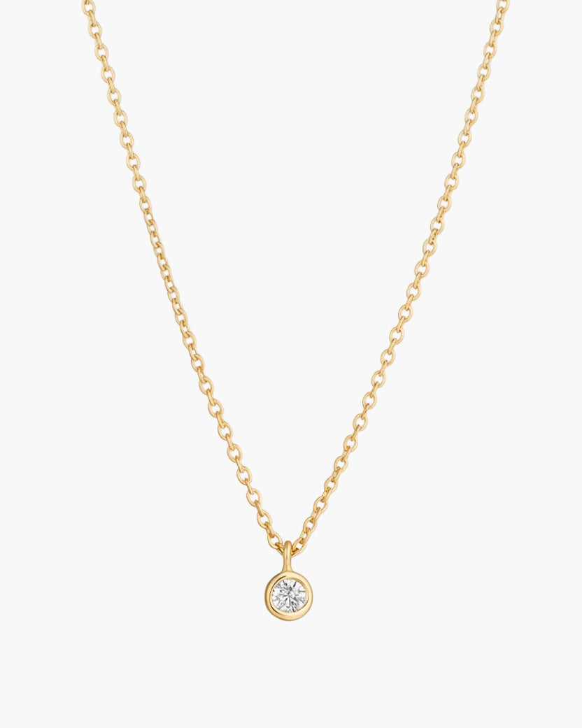 Gold dainty necklace with a diamond pendant on a white background