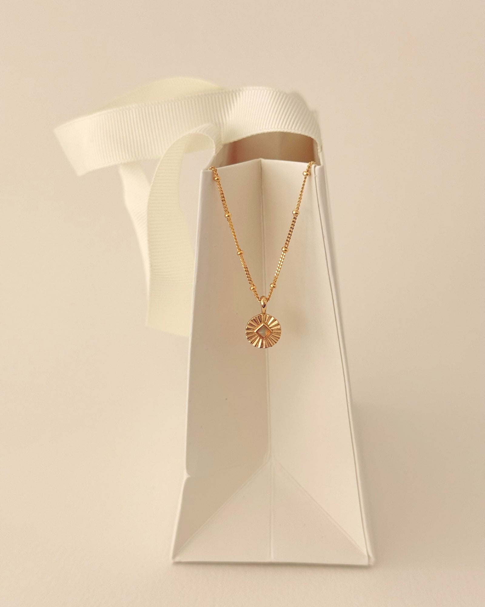 Gold necklace with a sunburst pendant on a white background