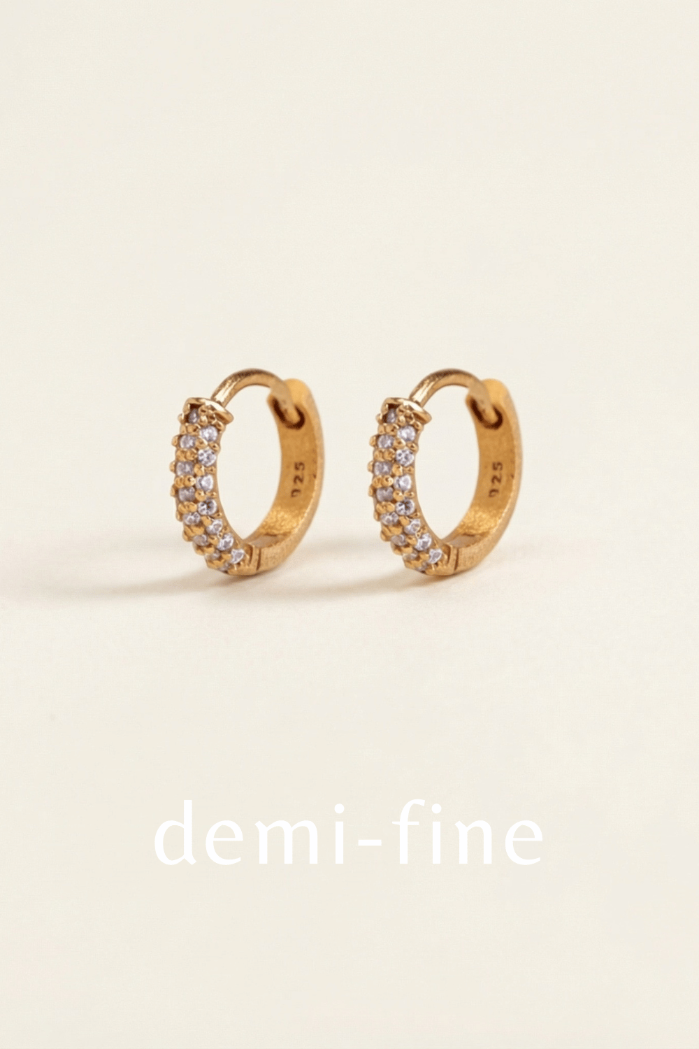 Gold hoop earrings with small cubic zirconia on a beige background, labeled 'demi-fine'.