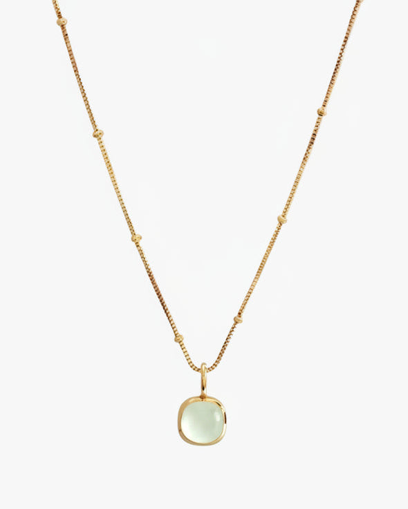 Gold necklace with a green pendant on a white background