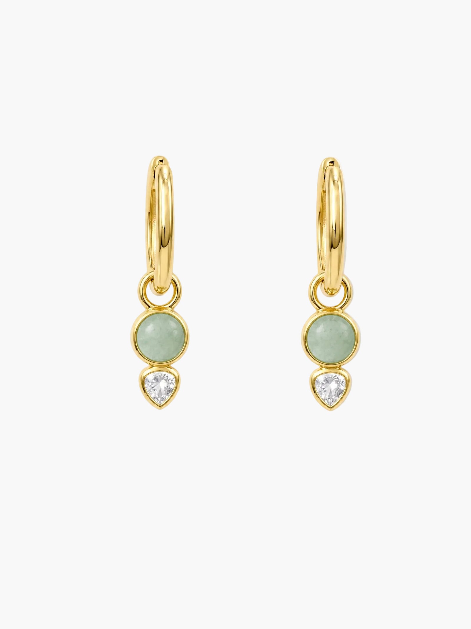 A pair of gold huggie hoop earrings with a light green oval stone, a clear heart-shaped crystal, and a small gold heart charm, shown on a white background.