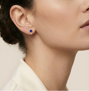 Close-up of a person wearing a blue gemstone earring on a neutral background