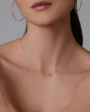 Woman wearing gold jewelry including a dainty necklace, large hoop earrings, and a pearl nugget bracelet against a neutral background