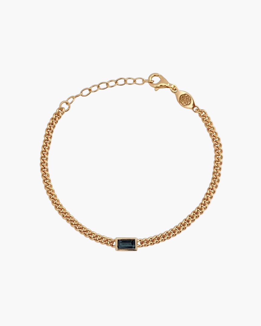 Gold bracelet with a blue rectangular gemstone on a light grey background