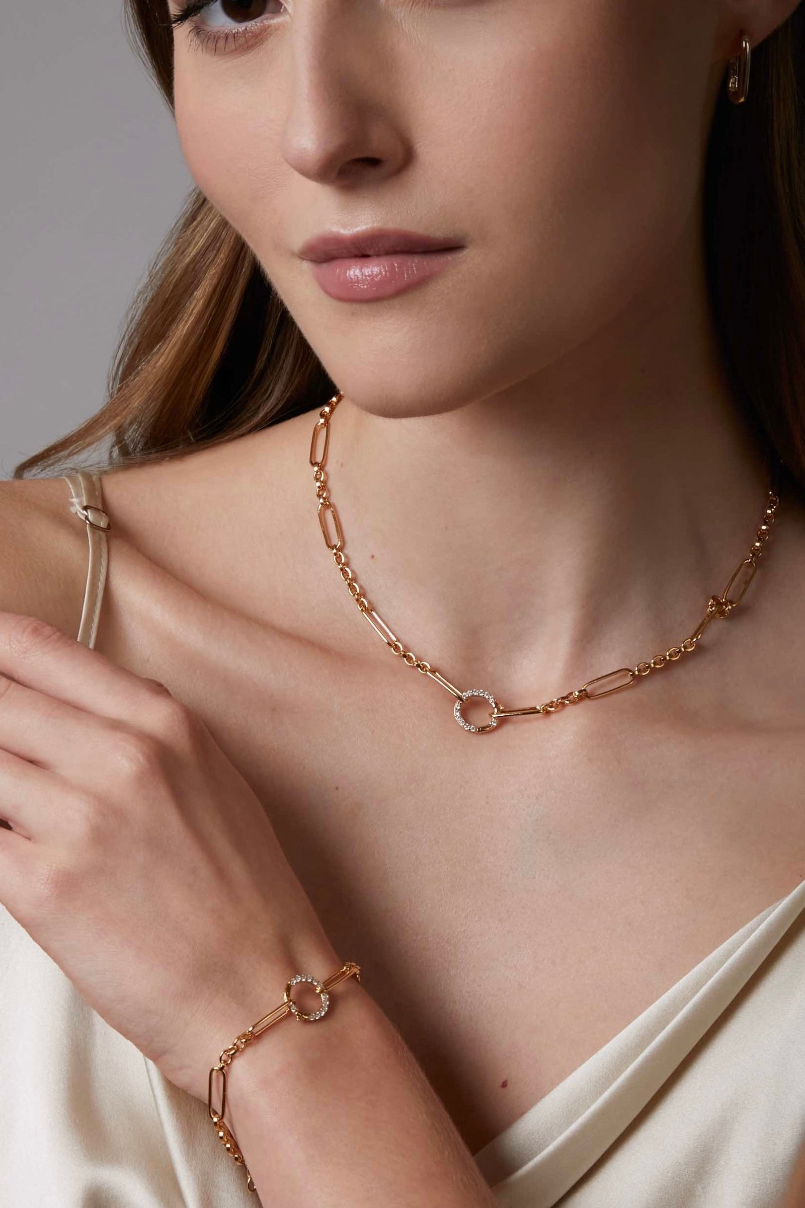 Woman wearing a gold necklace and bracelet against a neutral background