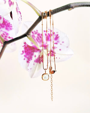 Delicate gold necklace with a heart pendant on a branch with pink flowers