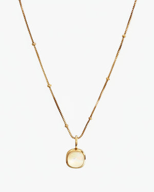 Gold necklace with a round pendant on a off white background