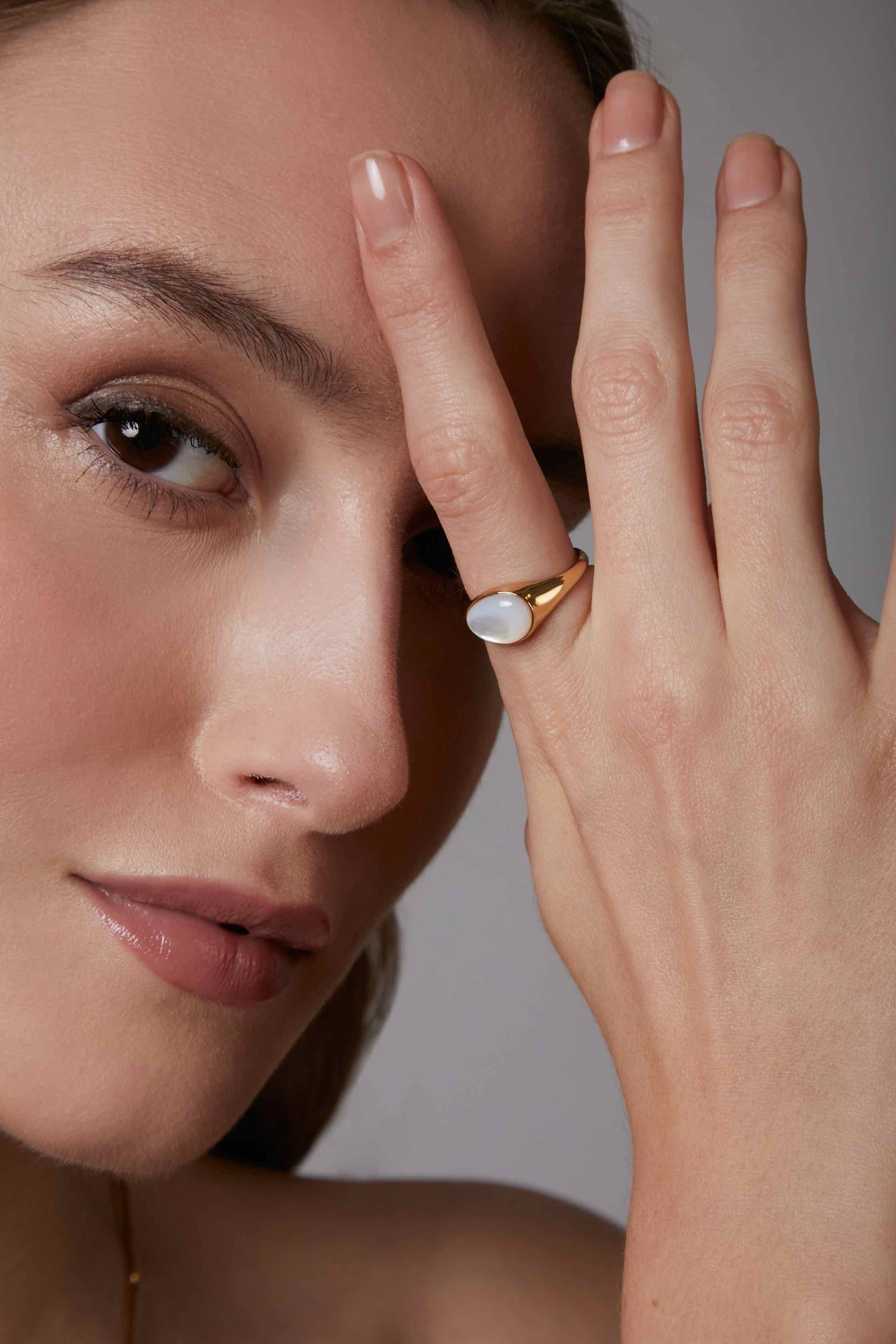 Close-up of a woman wearing gold mother of pearl cabochon rings on a neutral background.