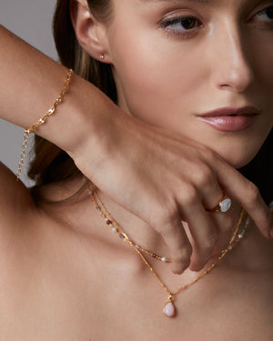 Woman wearing gold jewelry including a necklace, bracelet, and ring.