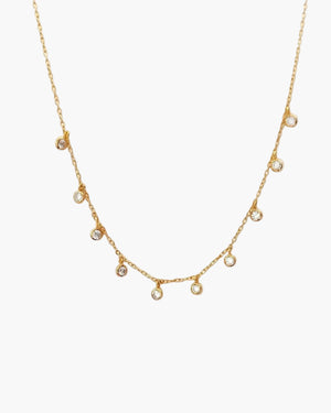 Gold necklace with small cz droplets on a light grey background