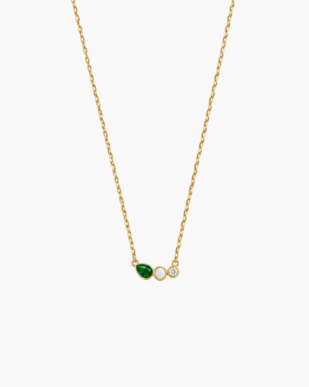 A delicate gold chain necklace featuring a small pendant with a green marquise-cut stone, a round white stone, and a tiny gold dot, displayed against a clean off-white background.