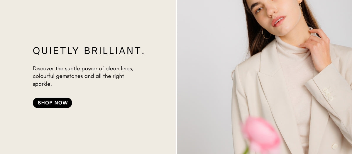 a woman wearing off white blazer and turtle neck on light background. She wears large gold hoop earrings