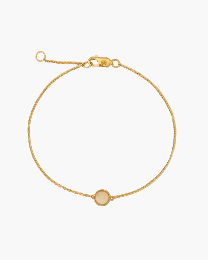 Gold bracelet with a small round charm on a white background